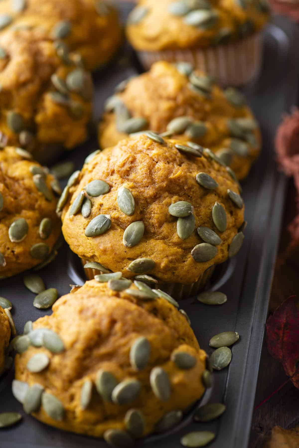 close up of pumpkin muffins topped with pumpkin seeds in a muffin pan