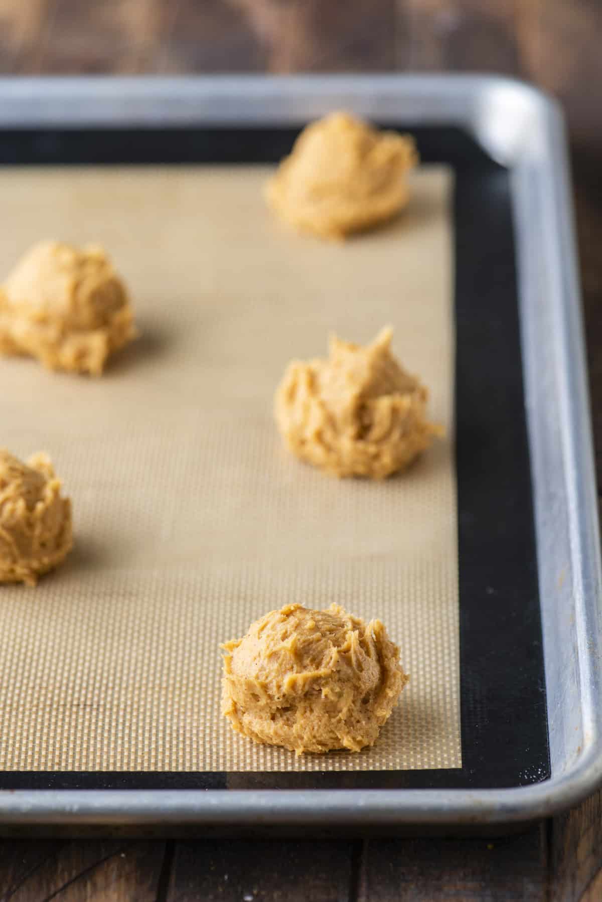 rows of pumpkin cookie dough balls on a baking sheet lined with a silicone baking mat