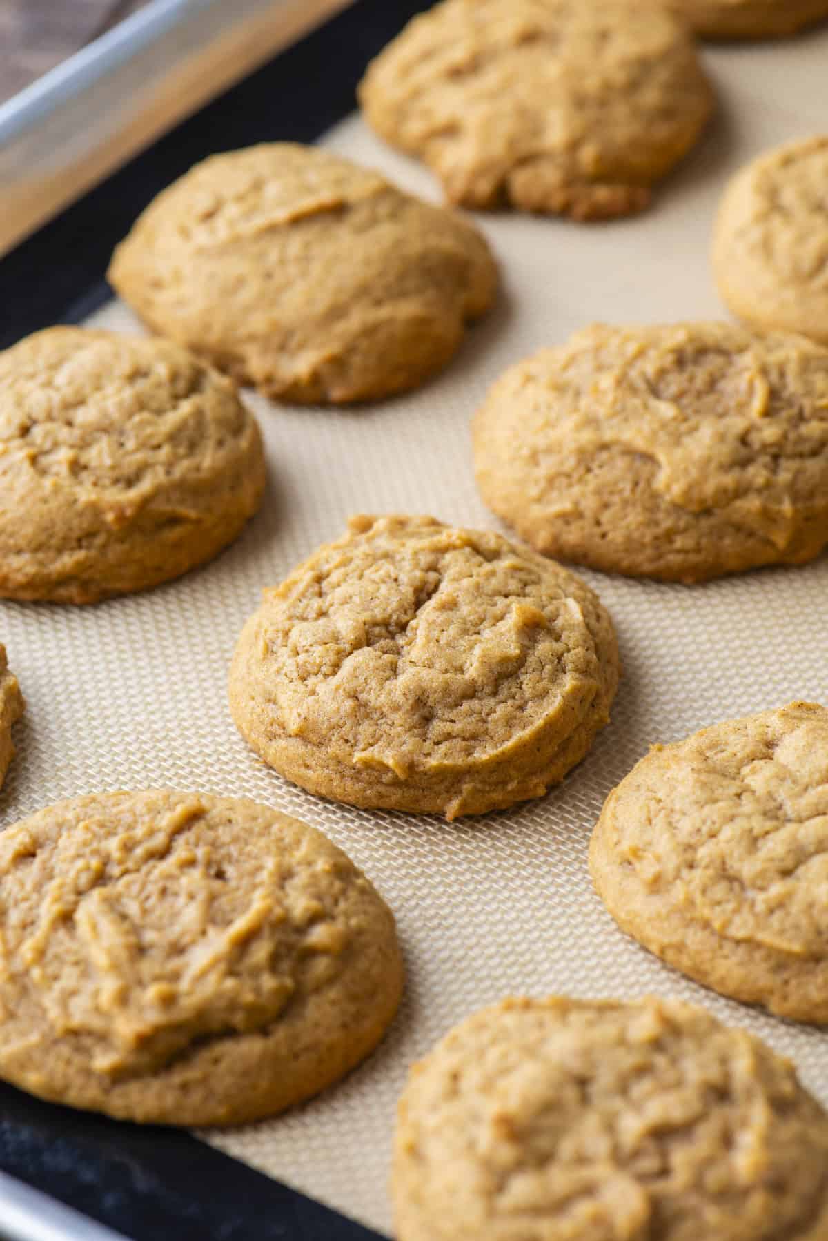 rows of freshly baked pumpkin cookies on a baking sheet lined with a silicone baking mat