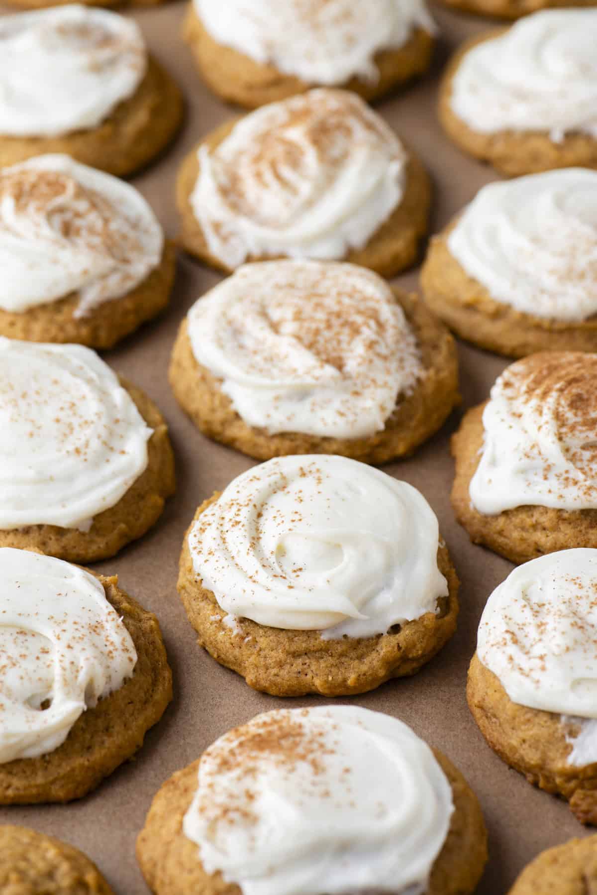 rows of pumpkin cookies with cream cheese frosting on brown parchment paper