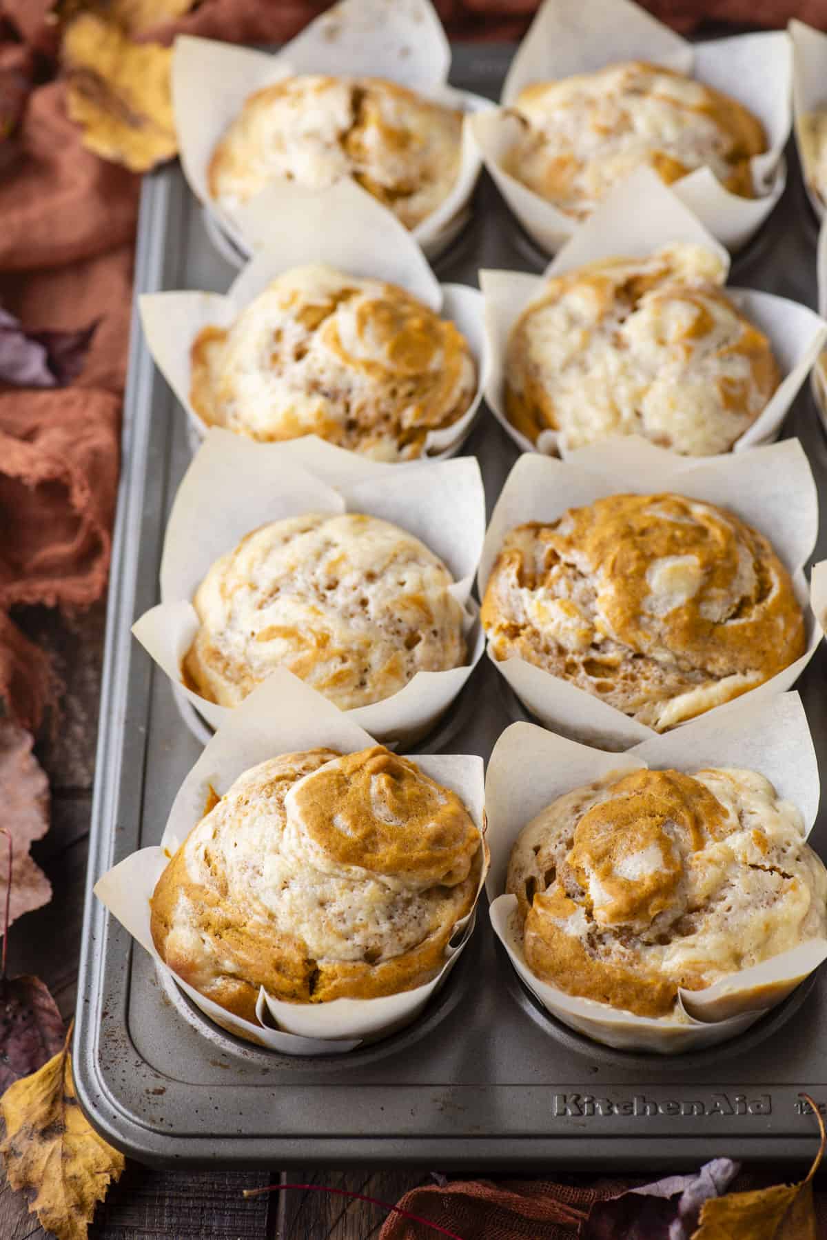 a muffin pan full of pumpkin cream cheese muffins in white liners