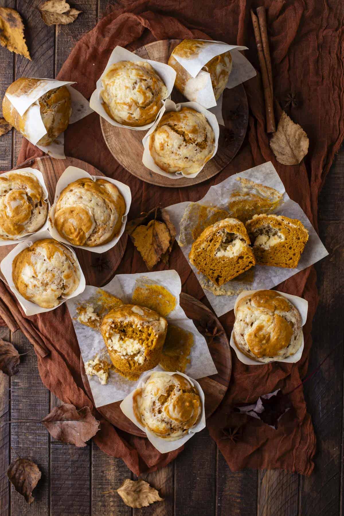 over head view of pumpkin cream cheese muffins scattered around, some upright, some on their sides cut in half, some with a bite missing, with fall leaves scattered around