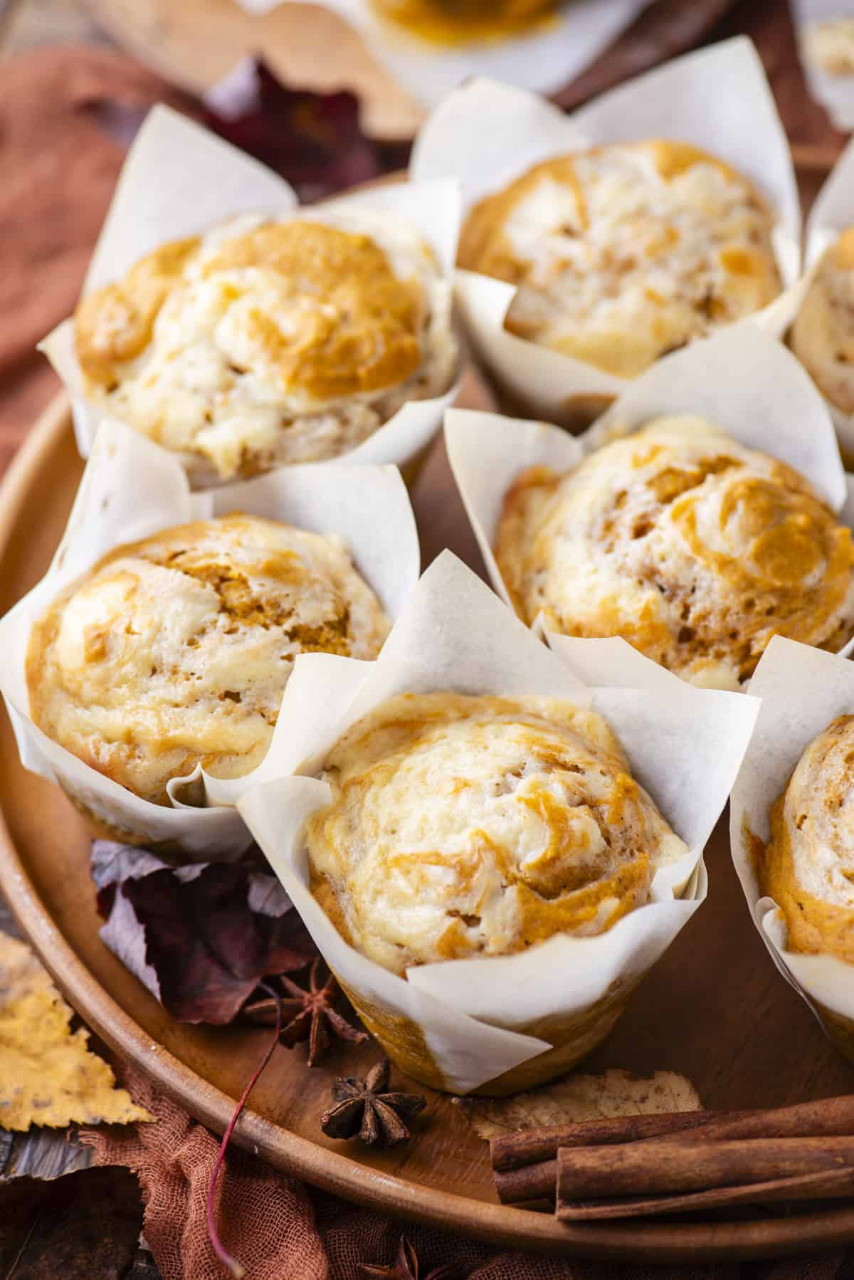 pumpkin cream cheese muffins in paper muffin cups on a wood platter surrounded by fall leaves