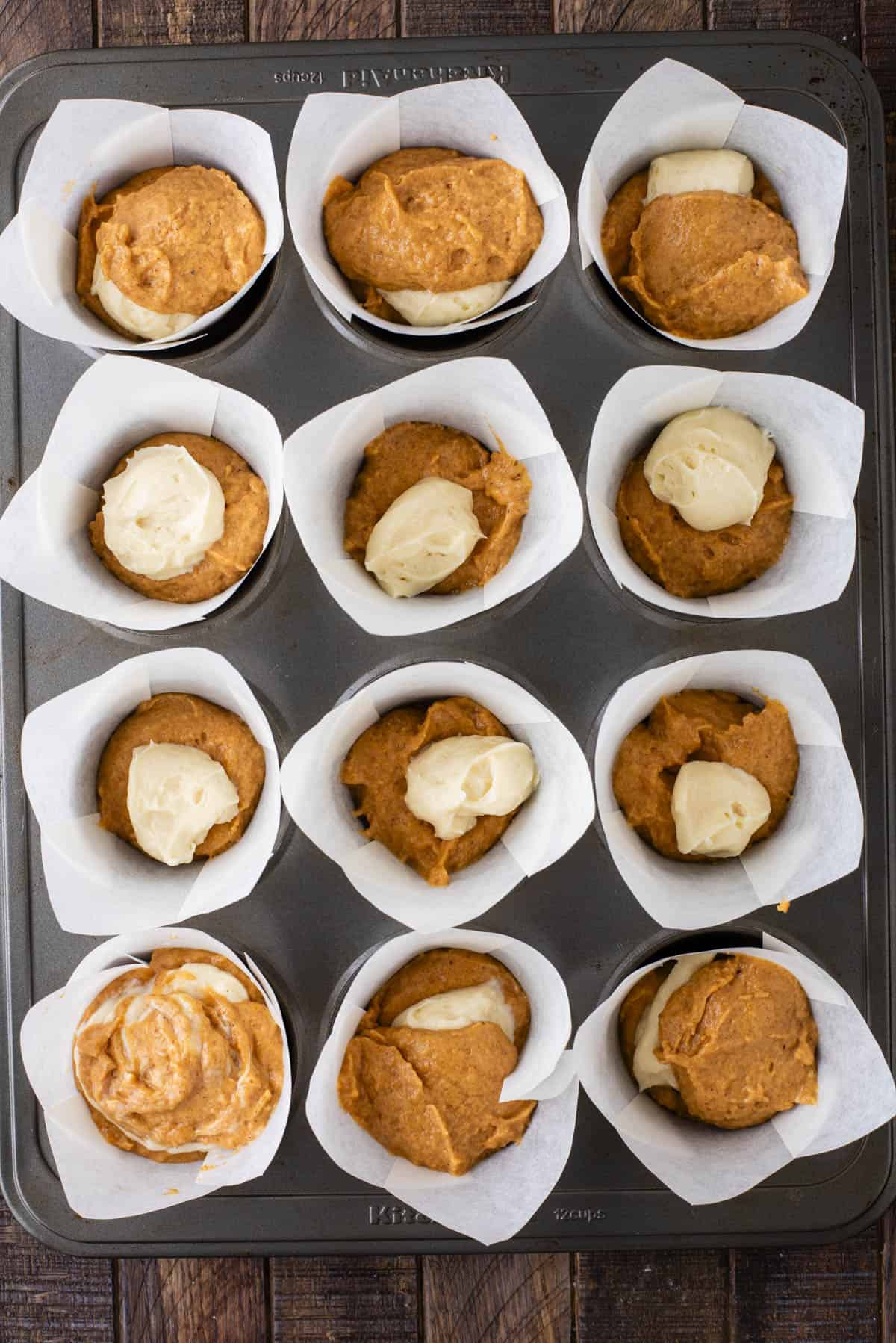 over head view of pumpkin muffin batter and cream cheese mixture layered in muffin liners in a muffin pan