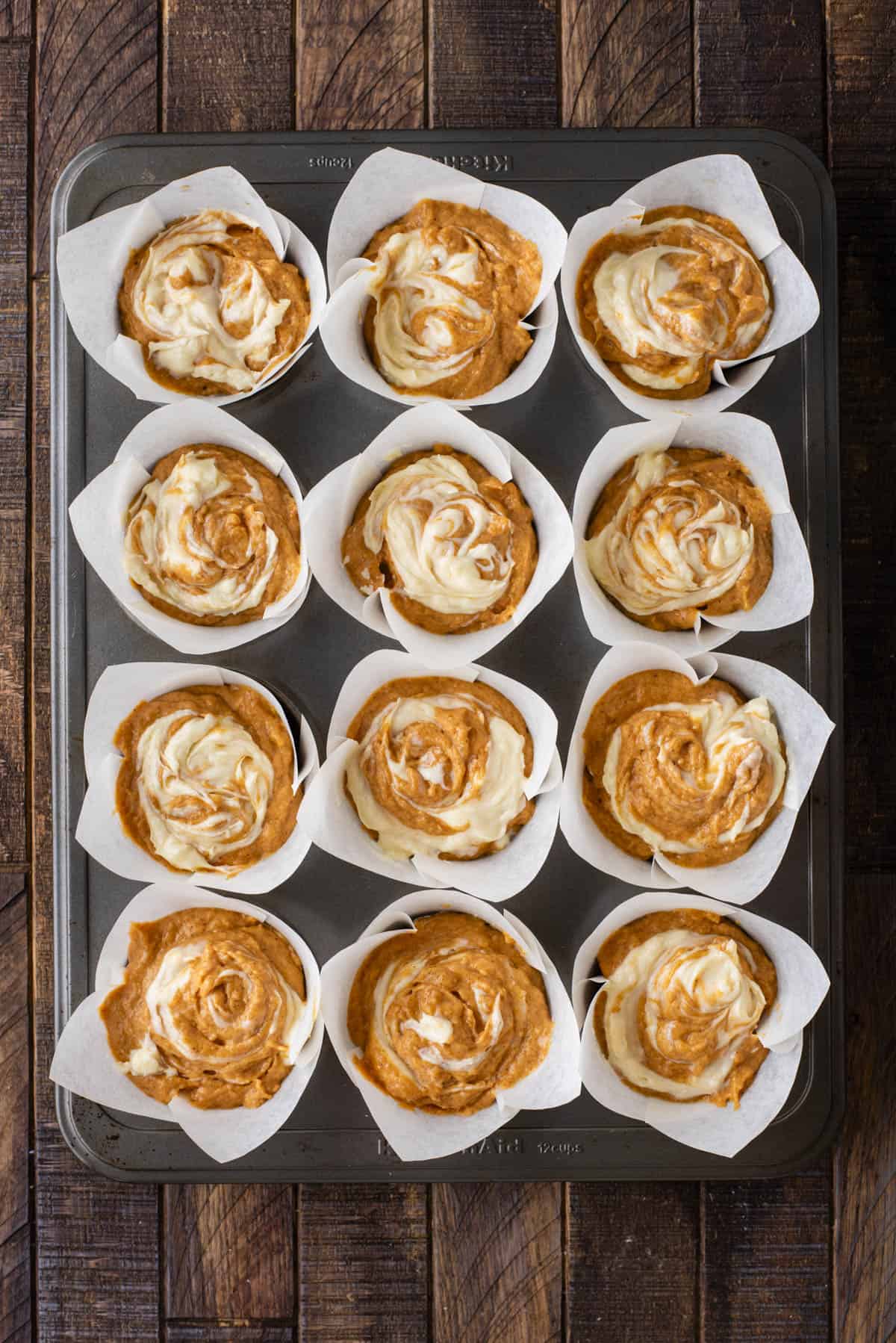 over head view of pumpkin cream cheese muffin batter in muffin liners in a muffin pan