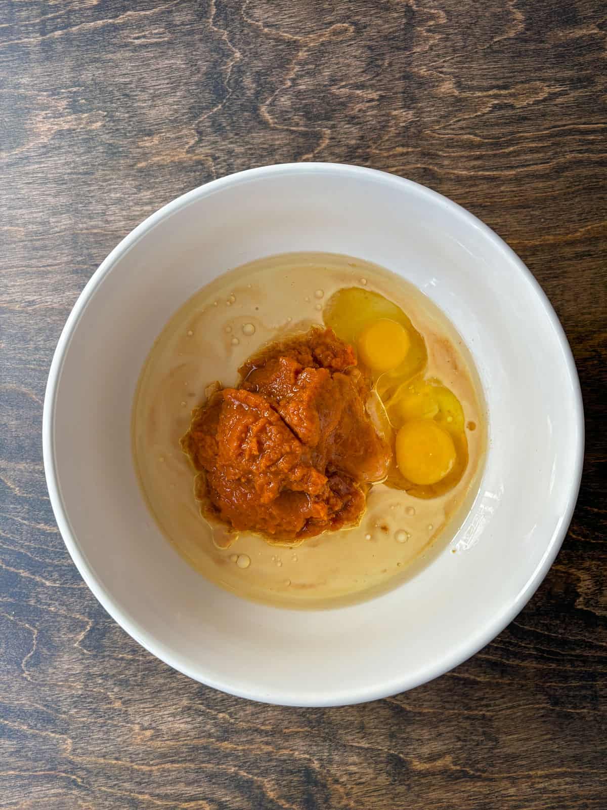 wet ingredients for pumpkin muffins including pumpkin puree, eggs and vegetable oil in a white bowl, not yet mixed together