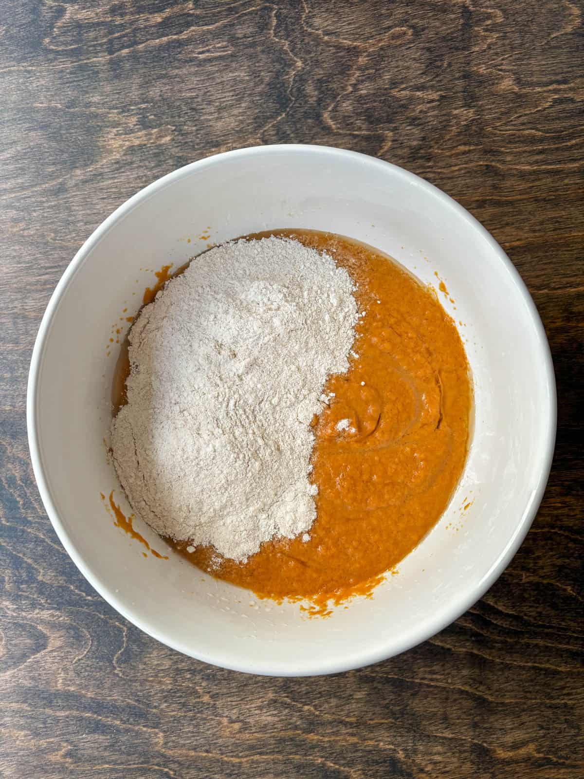 pumpkin puree mixture in a white bowl with a flour mixture on top, not yet mixed in