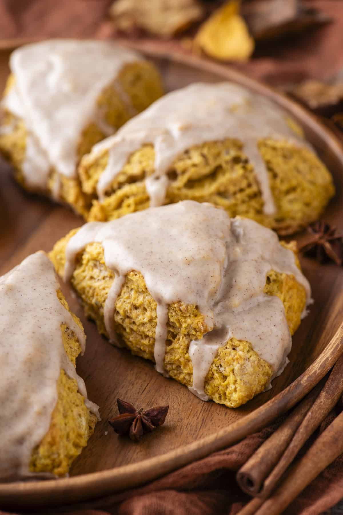 pumpkin scones on a wood plate with star anise, fall leaves and cinnamon sticks scattered around