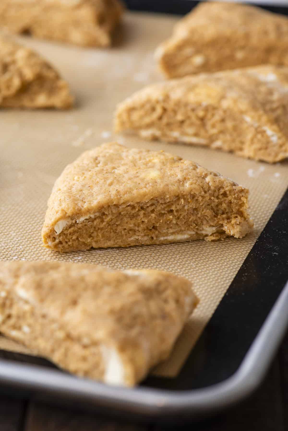 pumpkin scone dough cut in triangles in rows on a baking sheet lined with a silicone baking mat