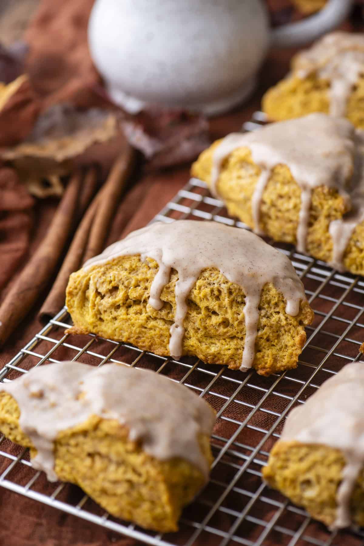 glazed pumpkin scones on a wire rack with fall leaves and cinnamon sticks scattered around below it