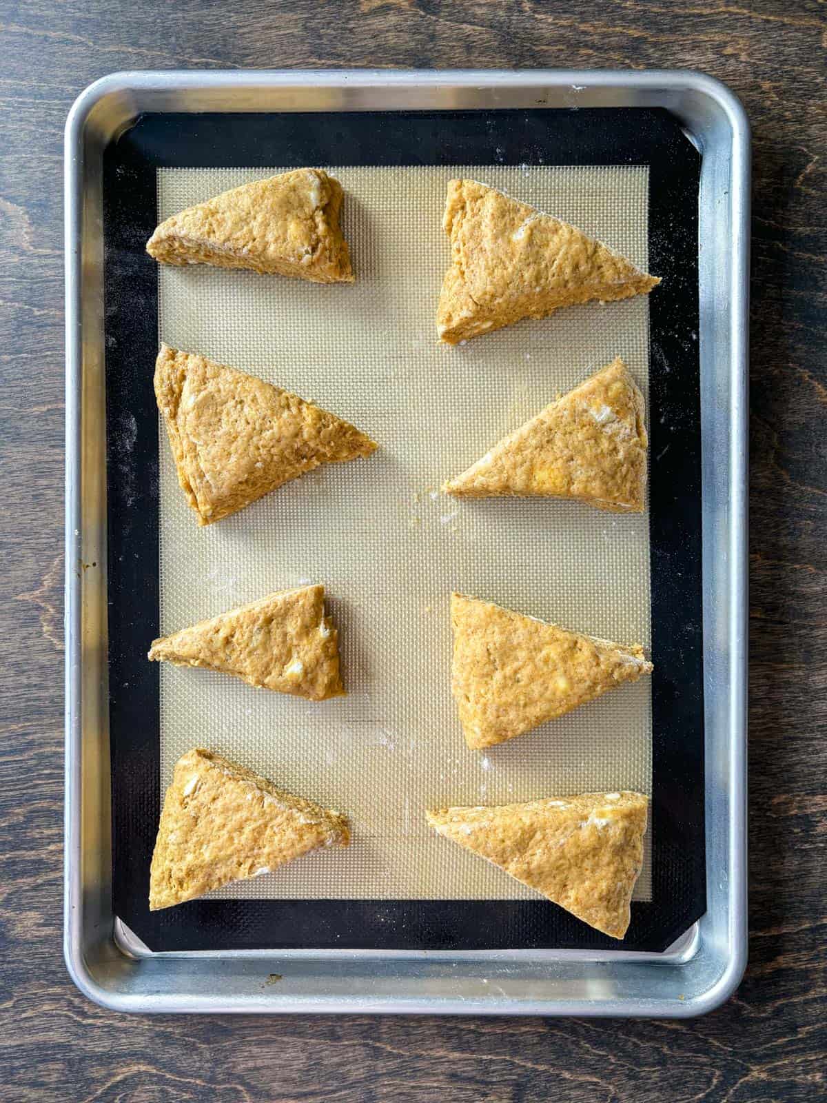 over head view of pumpkin scone dough in triangles on a baking sheet lined with a silicone baking mat