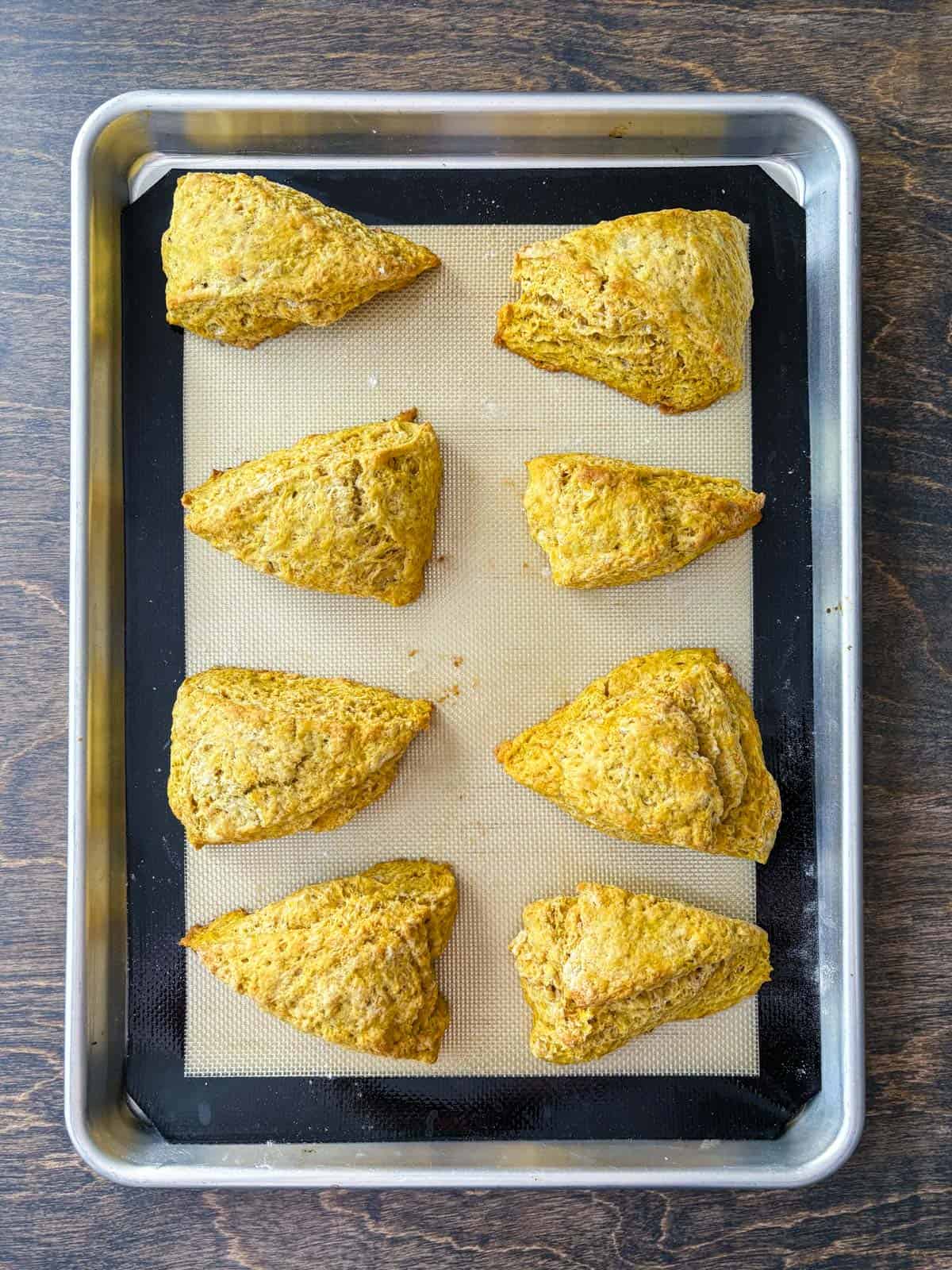 over head view of two rows of pumpkin scones on a baking sheet lined with a silicone baking mat