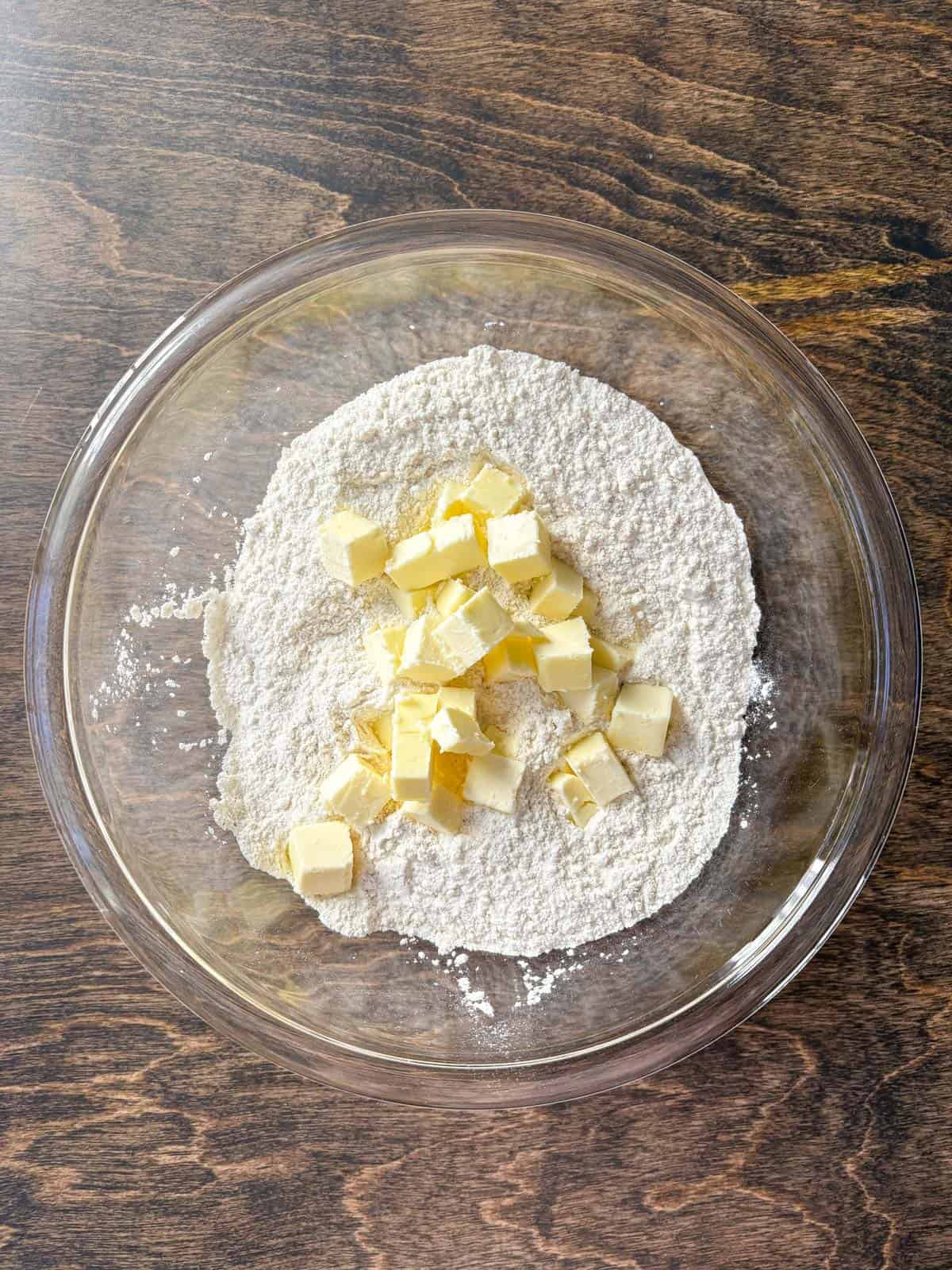 over head view of a clear glass bowl with a flour mixture and cubes of butter