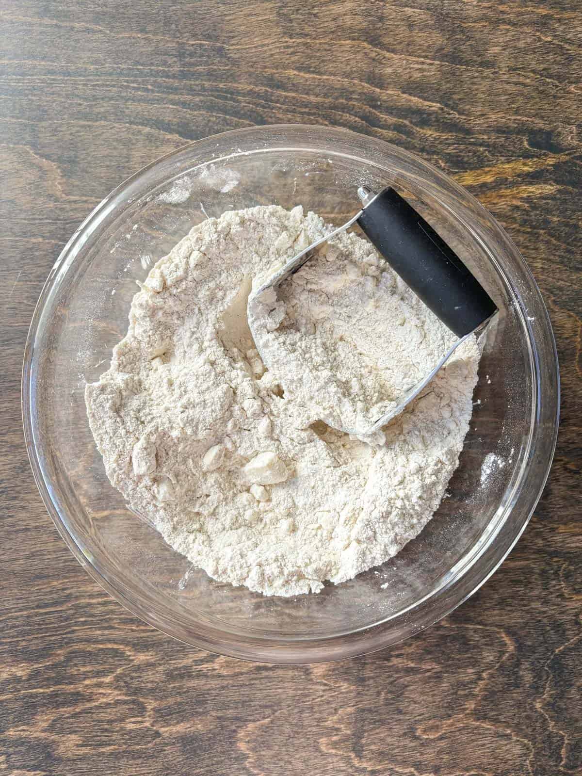 over head view of a clear glass bowl with a flour mixture and cubed cold butter with a pastry cutter