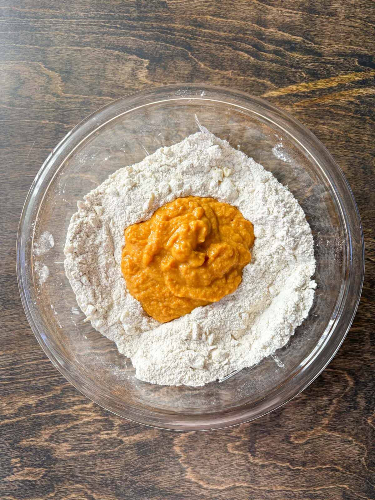 over head view of a clear glass bowl with a flour mixture and a pumpkin puree mixture in the middle, not yet mixed together