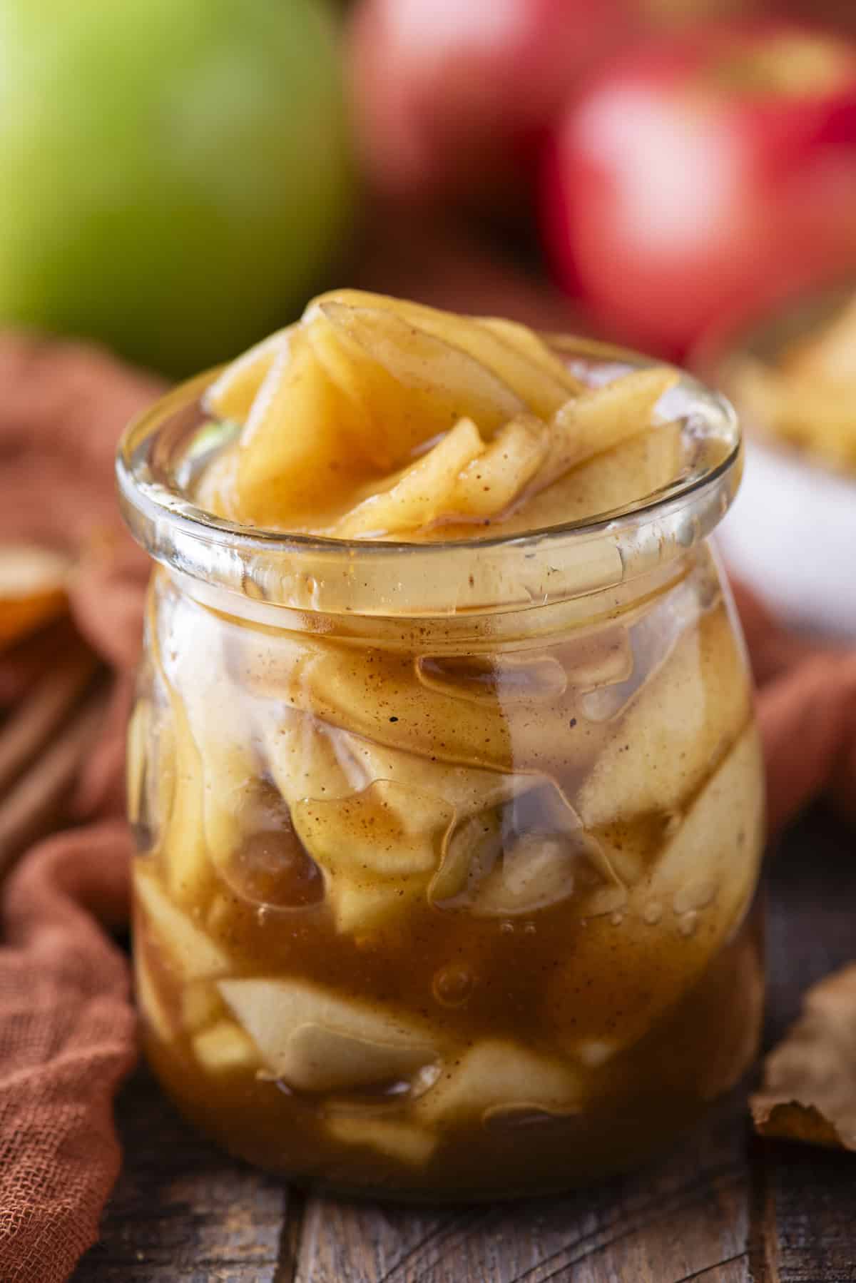 a small glass jar full of apple pie filling with red and green apples in the background