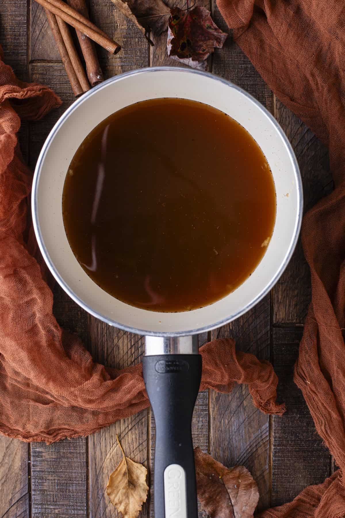 over head view of a small saucepan full of syrup, surrounded by fall leaves and cinnamon sticks