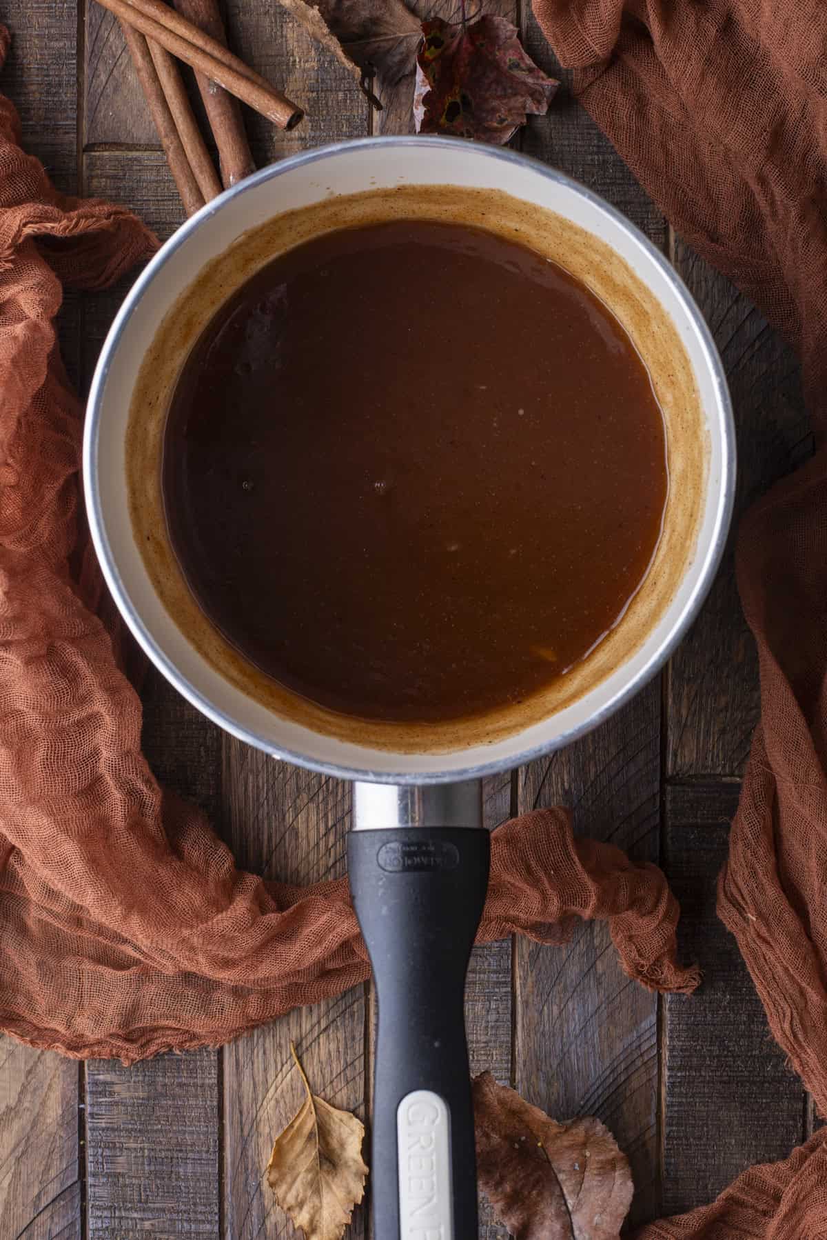 over head view of syrup in a saucepan surrounded by cinnamon sticks and fall leaves