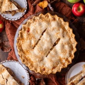 over head view of an apple pie surrounded by small plates with slices of pie