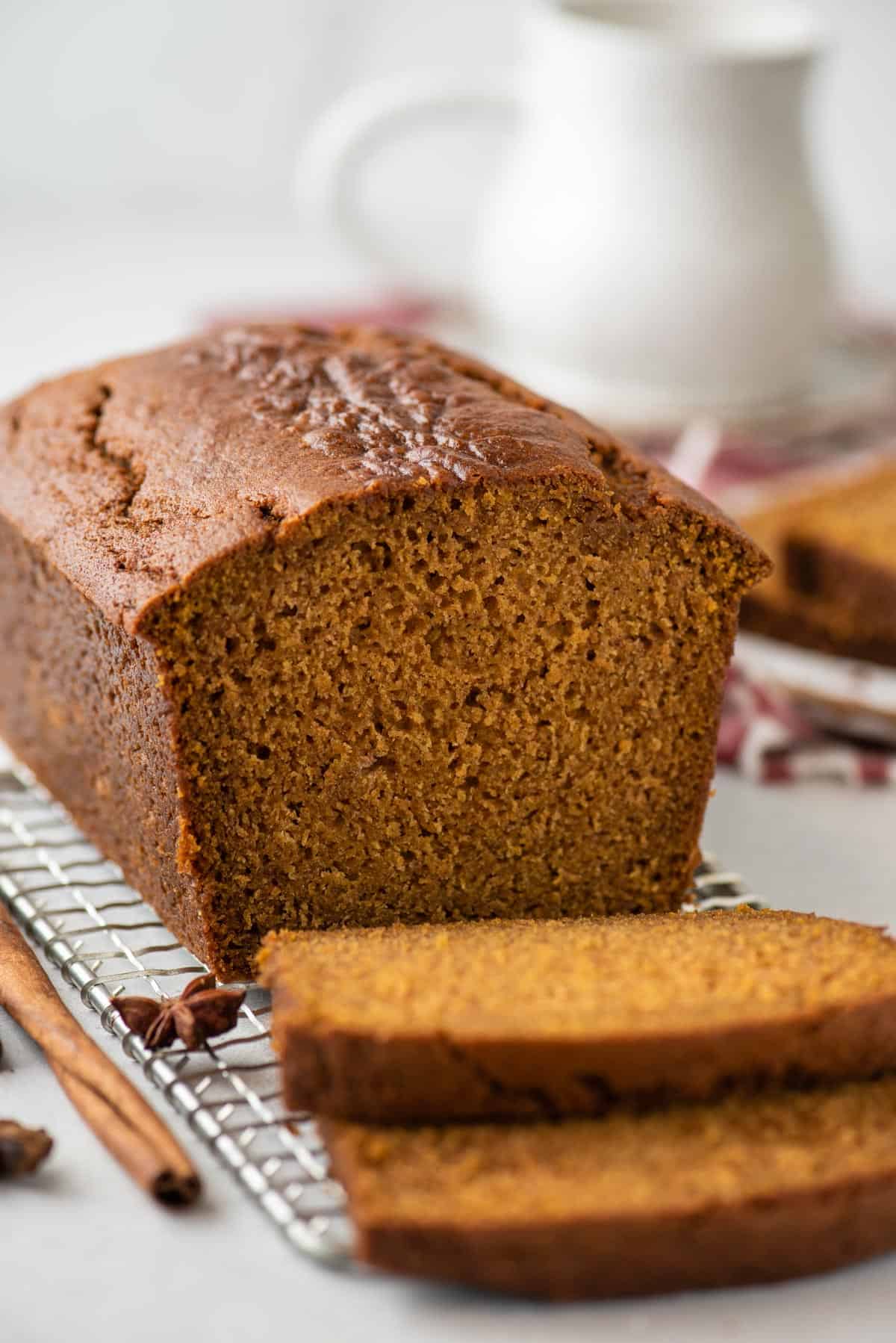 a loaf of pumpkin bread on a wire rack, with two slices cut laying by the loaf, a cinnamon stick and star anise scattered around