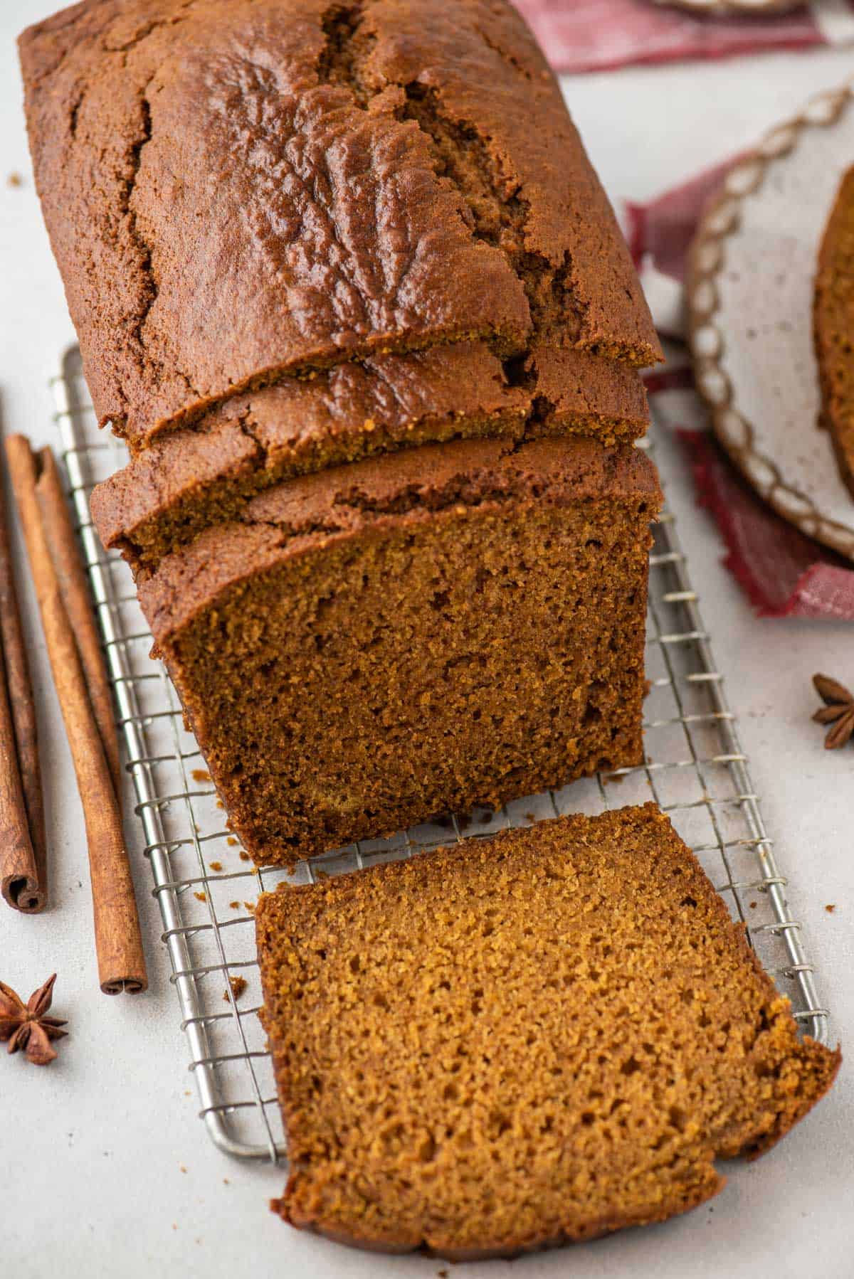 over head view of a loaf of pumpkin bread on a wire rack with three slices cut, two leaning on the rest of the loaf and one laying flat on the wire rack, cinnamon sticks and star anise scattered around