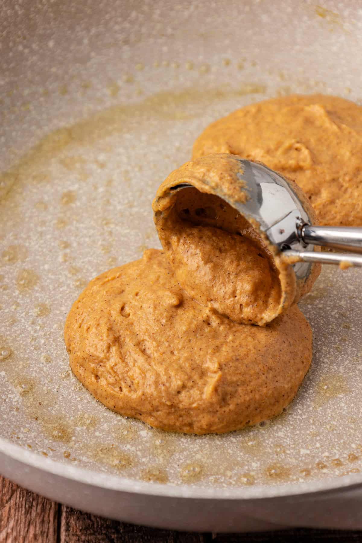 pumpkin pancake batter being placed into a pan with a cookie scoop