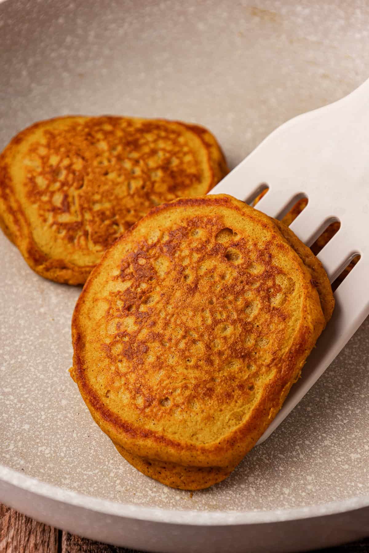 two pumpkin pancakes in a pan with one being lifted by a spatula