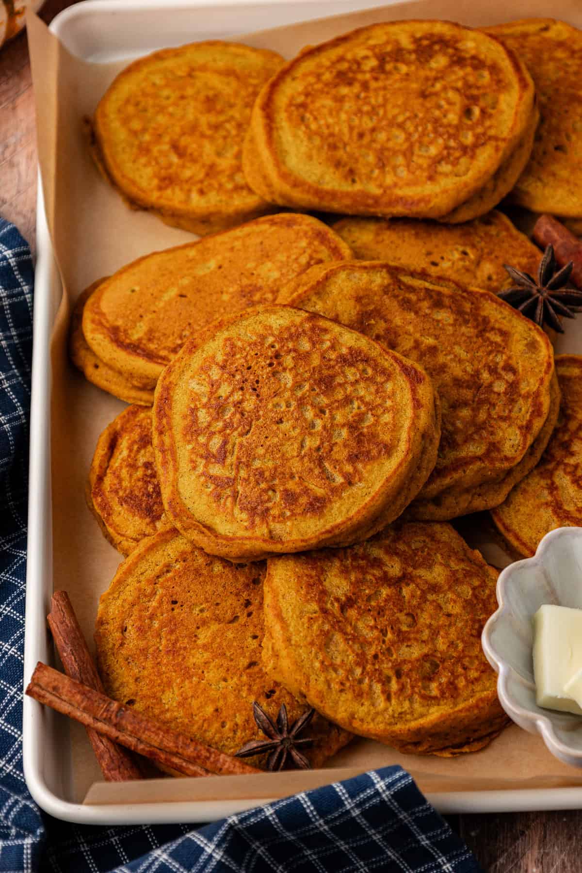 pumpkin pancakes piled in a baking sheet with scattered cinnamon sticks and star anise