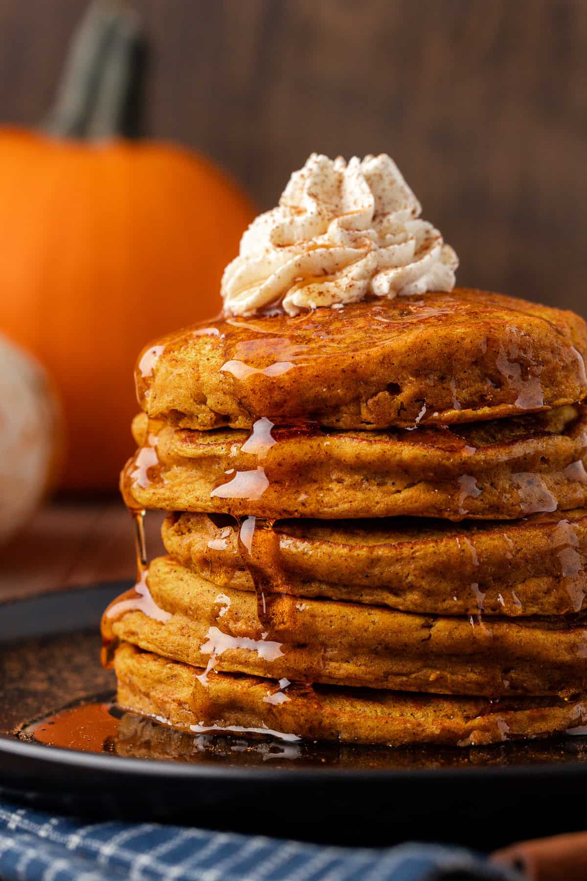 a stack of pumpkin pancakes on a black plate, topped with whipped cream and syrup