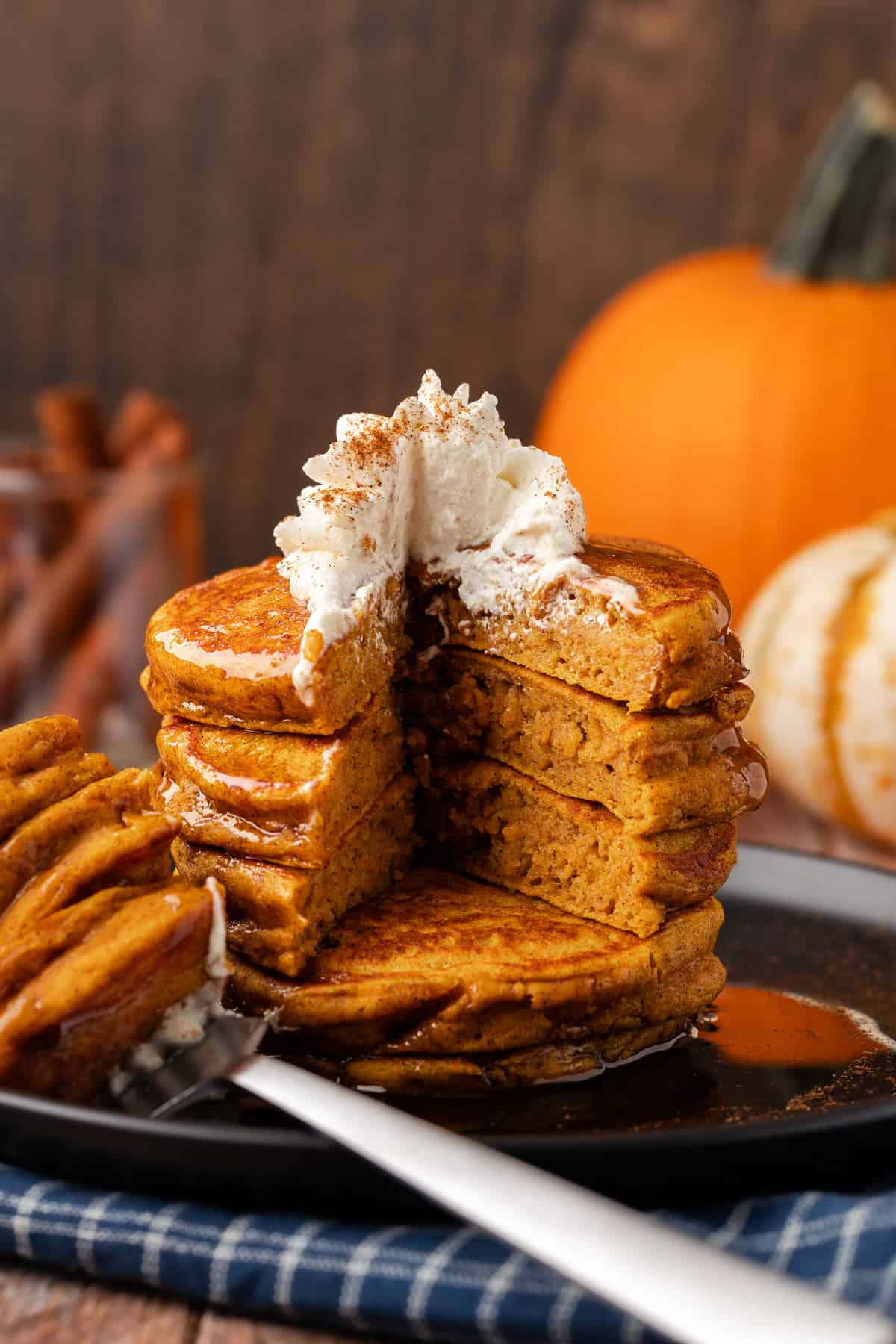 a stack of pumpkin pancakes on a plate with one wedged slice missing from three layers of pancakes