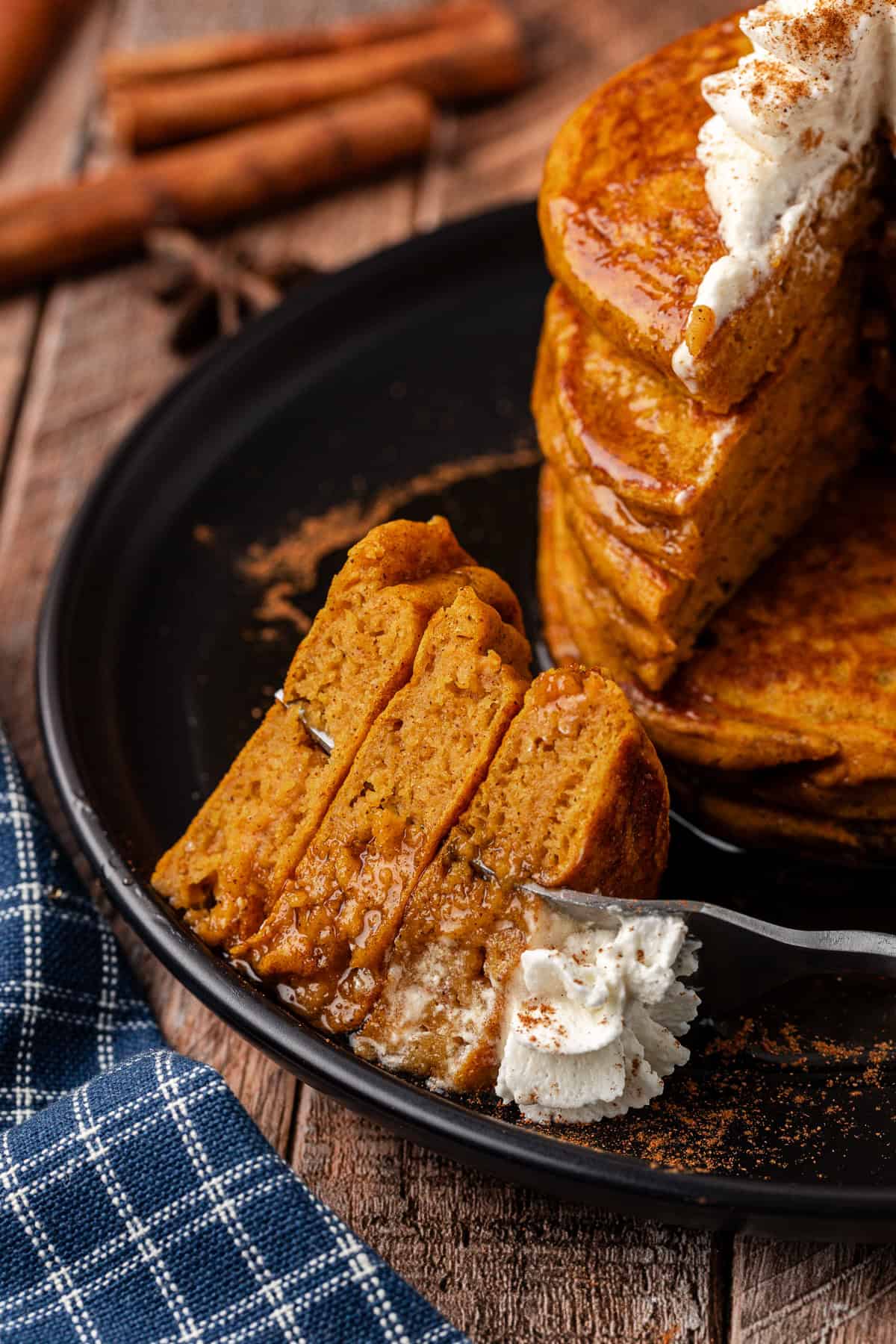 a black plate with a stack of pumpkin pancakes on it, with a fork with three pieces of pancake on it laying on the plate