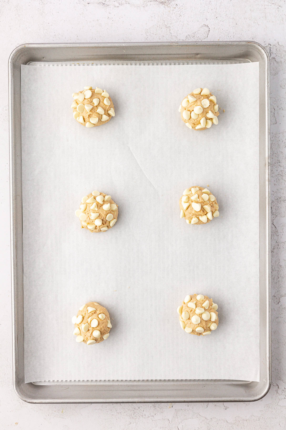 two rows of three white chocolate chip cookie dough balls on a baking sheet lined with white parchment paper