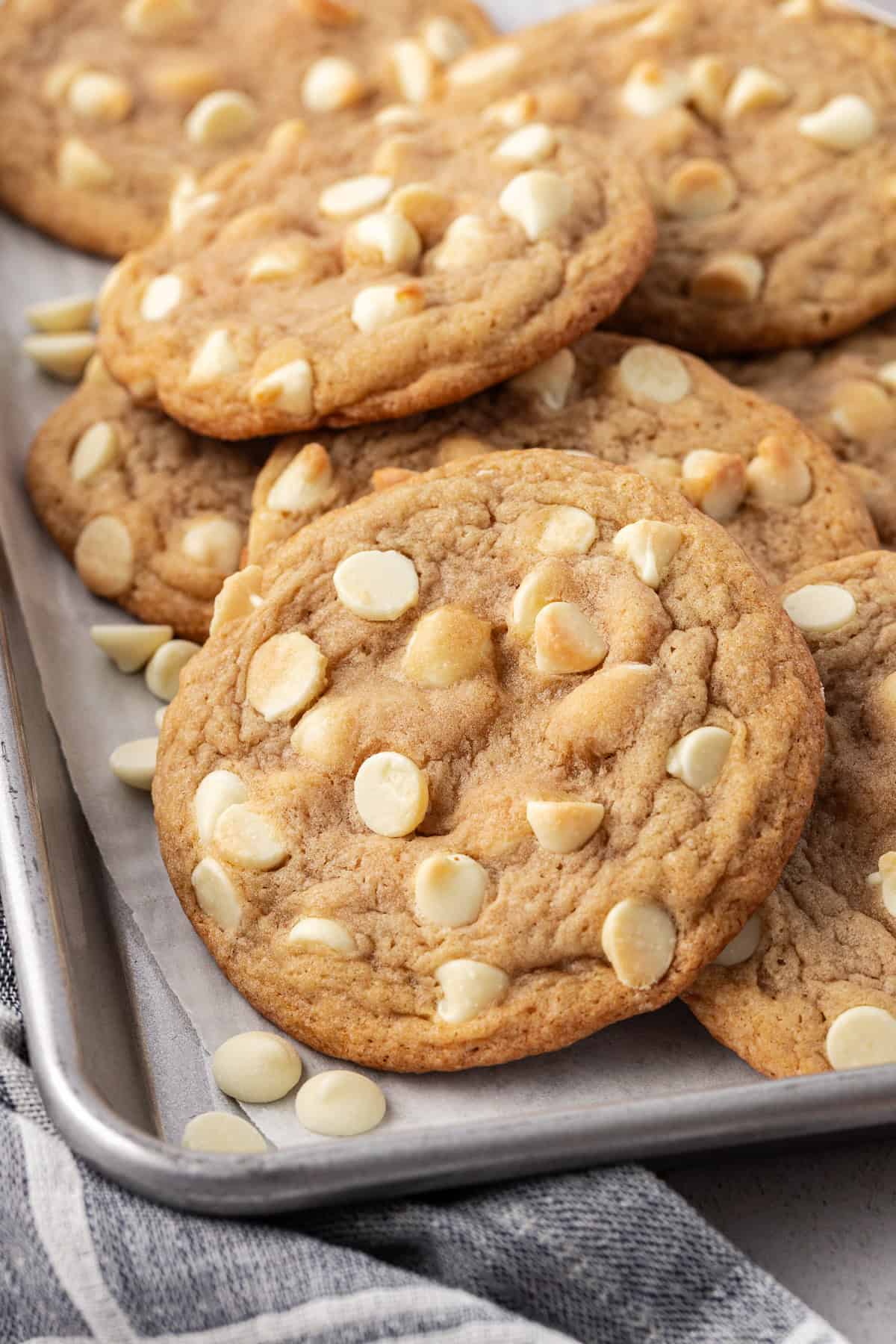 white chocolate chip cookies piled and scattered on a baking sheet