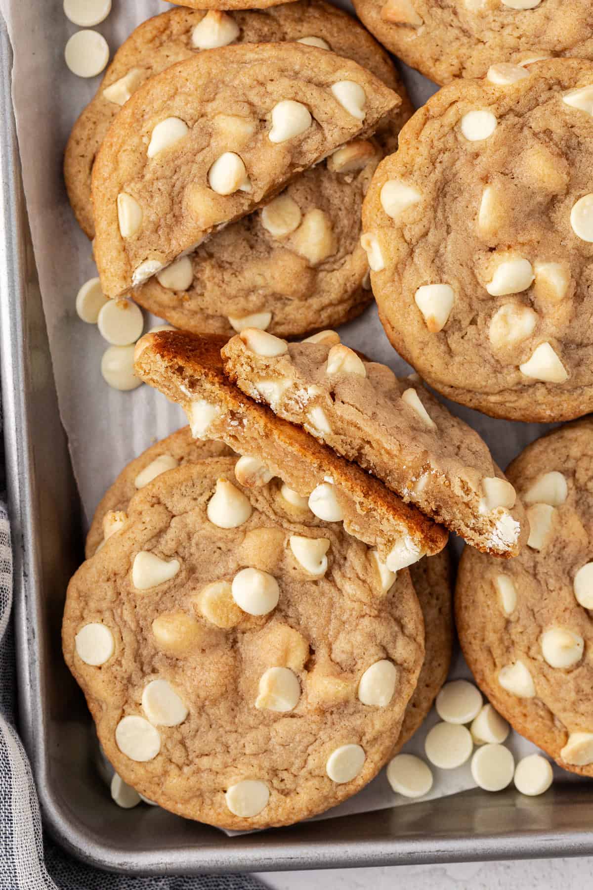 white chocolate chip cookies and white chocolate chips piled and scattered on a baking sheet