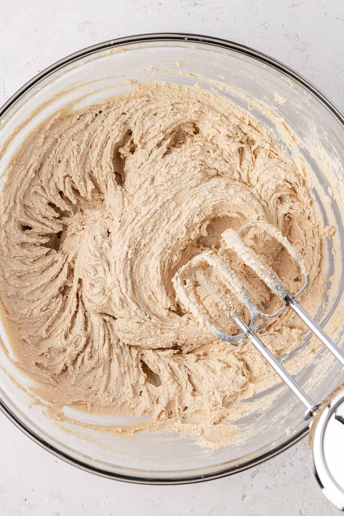 cookie dough batter in a clear glass bowl with an electric mixer leaning on the side of the bowl