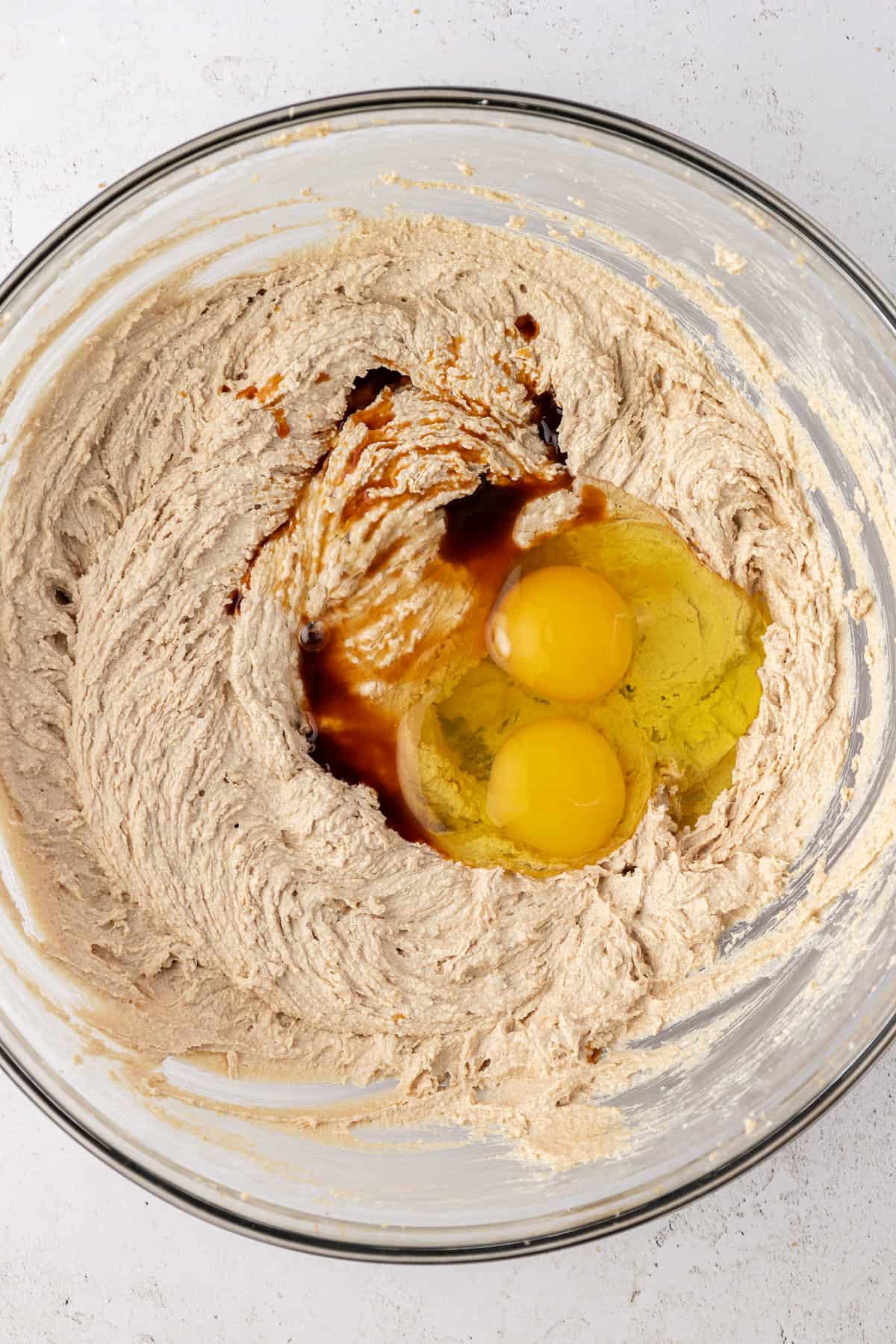 white chocolate chip cookie dough ingredients in a clear glass bowl, with egg and vanilla sitting on top not yet combined