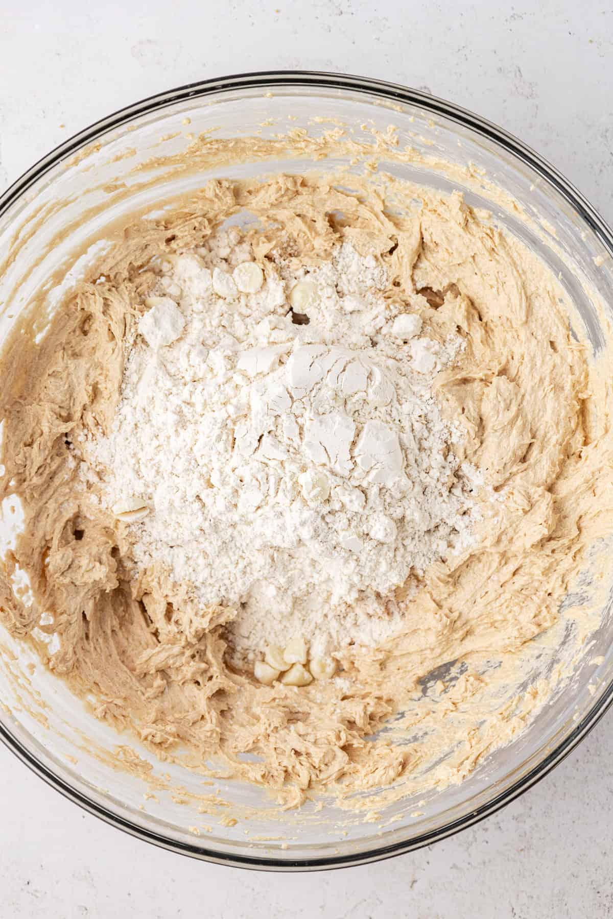 white chocolate chip cookie dough ingredients in a clear glass bowl, not yet completely combined so the flour mixture is sitting in a pile on top