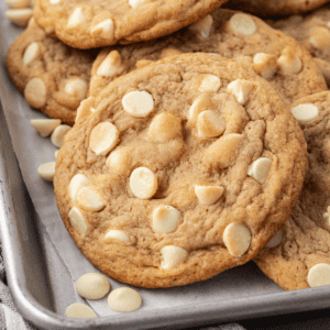 white chocolate chip cookies and white chocolate chips piled and scattered on a baking sheet