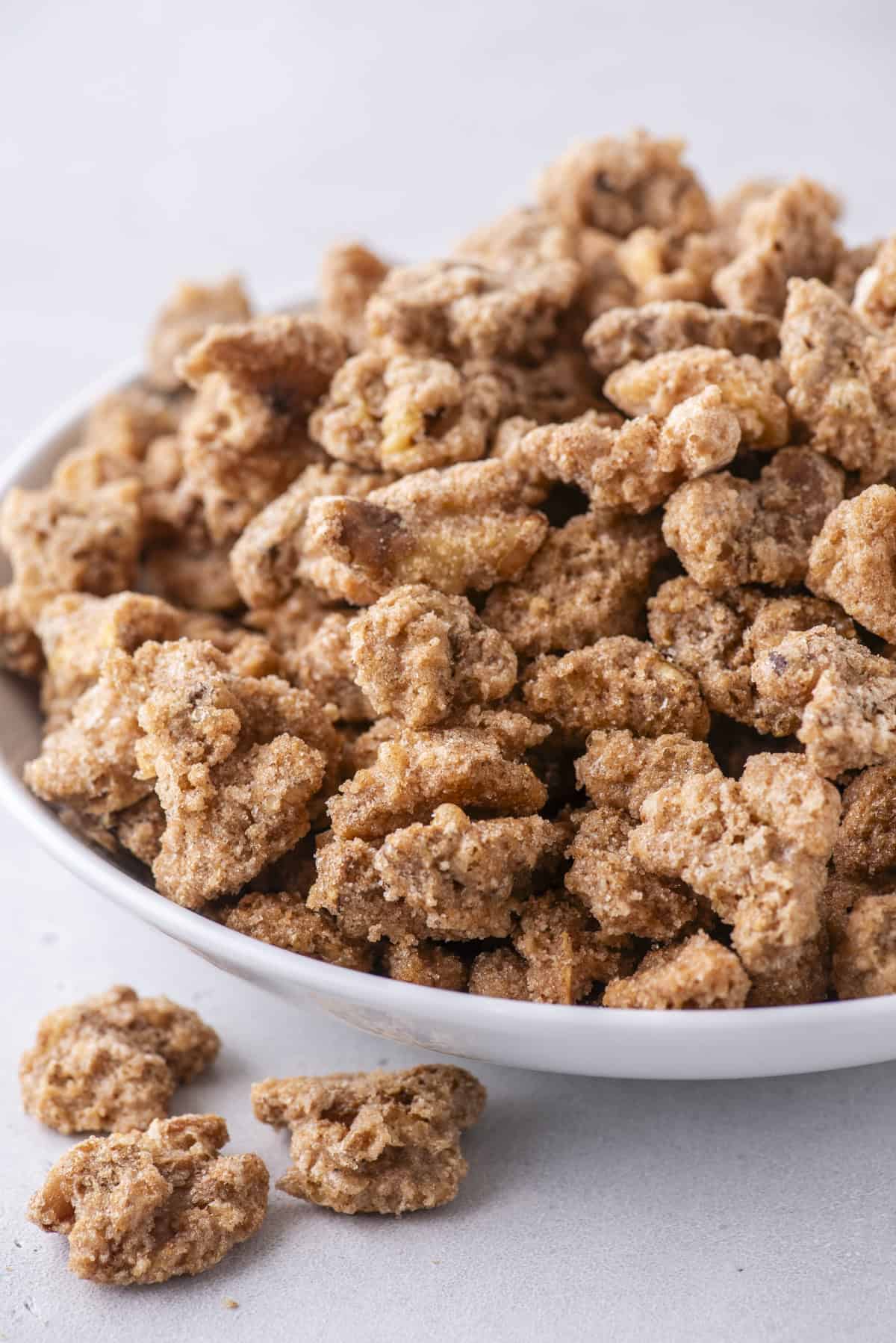 candied walnuts in a white bowl, with three more outside the bowl