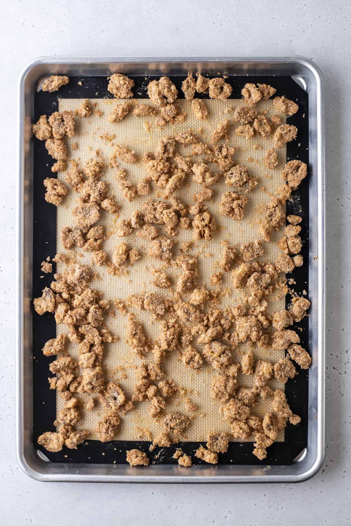 candied walnuts spread onto a baking sheet lined with a silicone baking mat