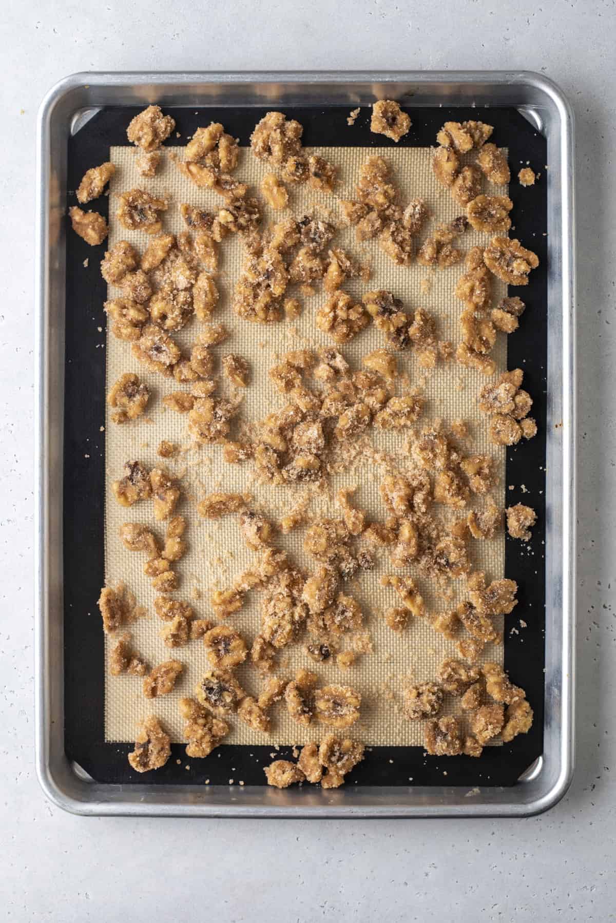 candied walnuts spread onto a baking sheet lined with a silicone baking mat