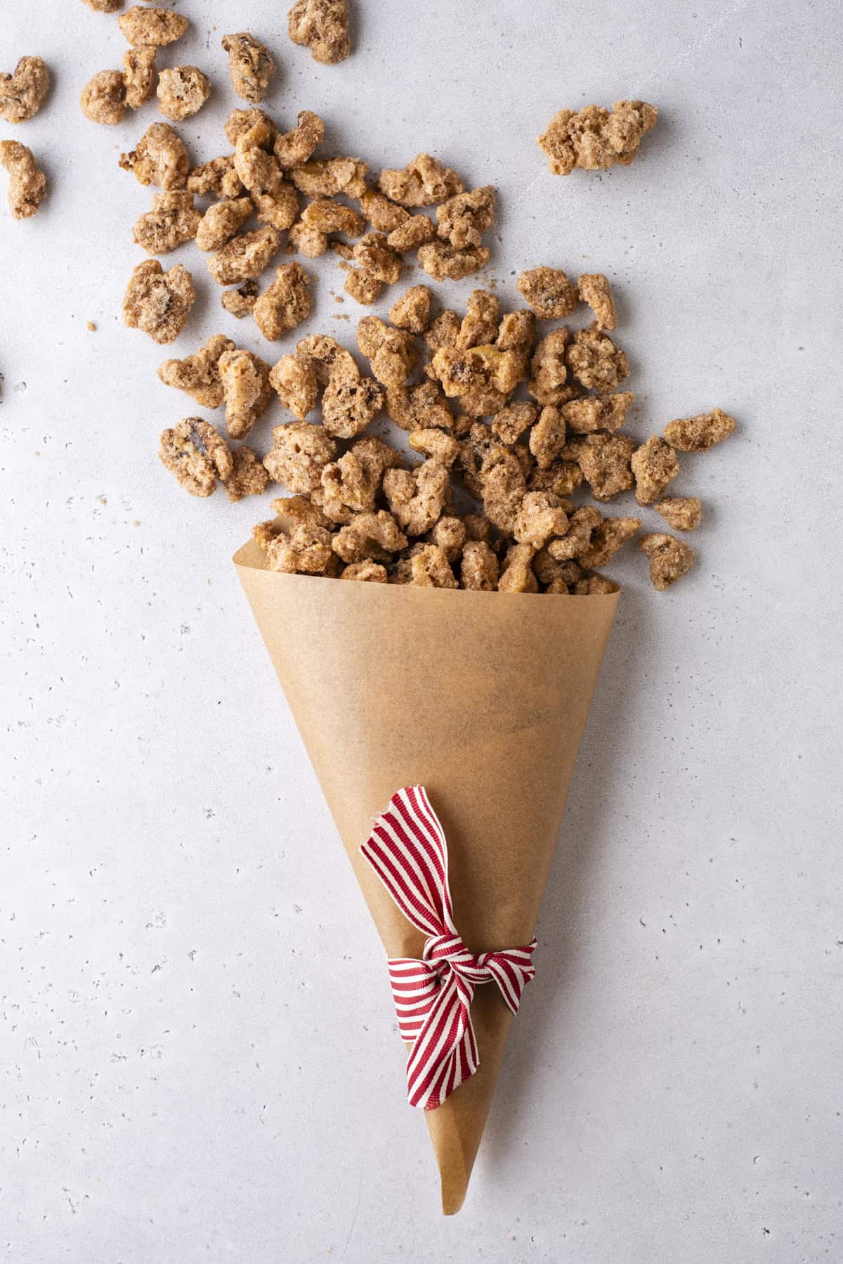 candied walnuts spilling out of a brown paper cone with a red and white striped ribbon tied around it