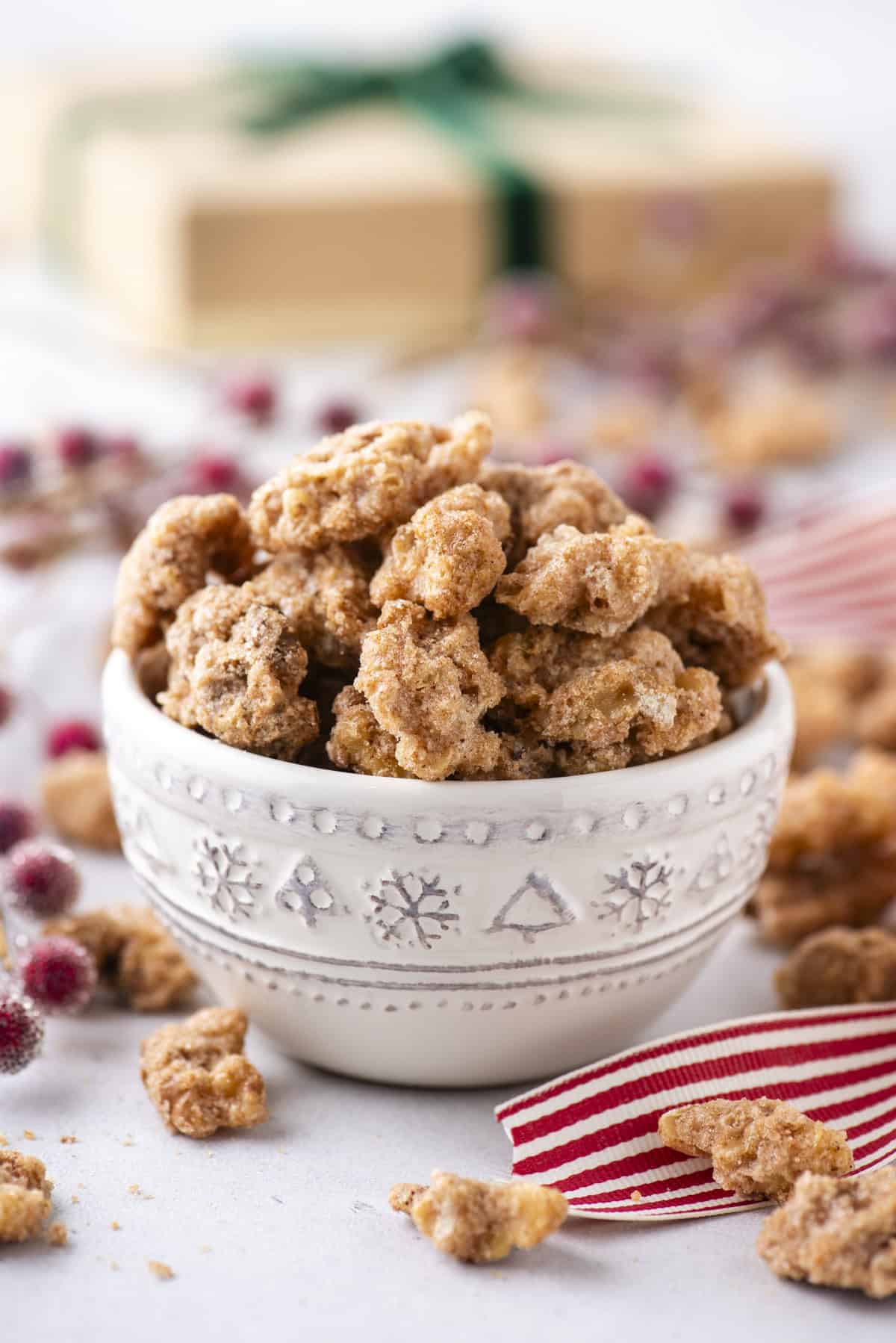 candied walnuts in a small white bowl with more scattered around and a red and white striped ribbon