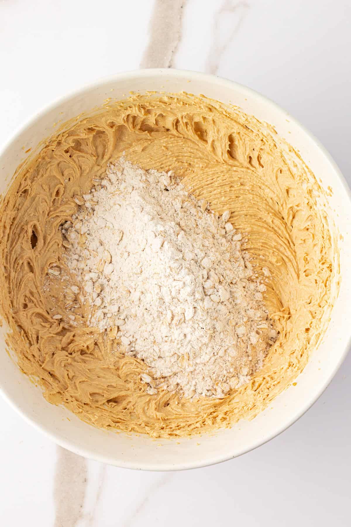 over head view of peanut butter oatmeal cookie dough ingredients in a large white bowl