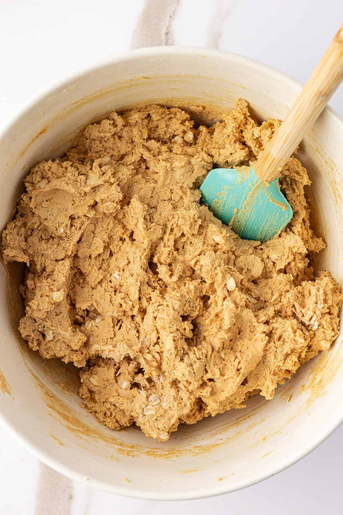 peanut butter oatmeal cookie dough in a large white bowl with a teal and wood spatula