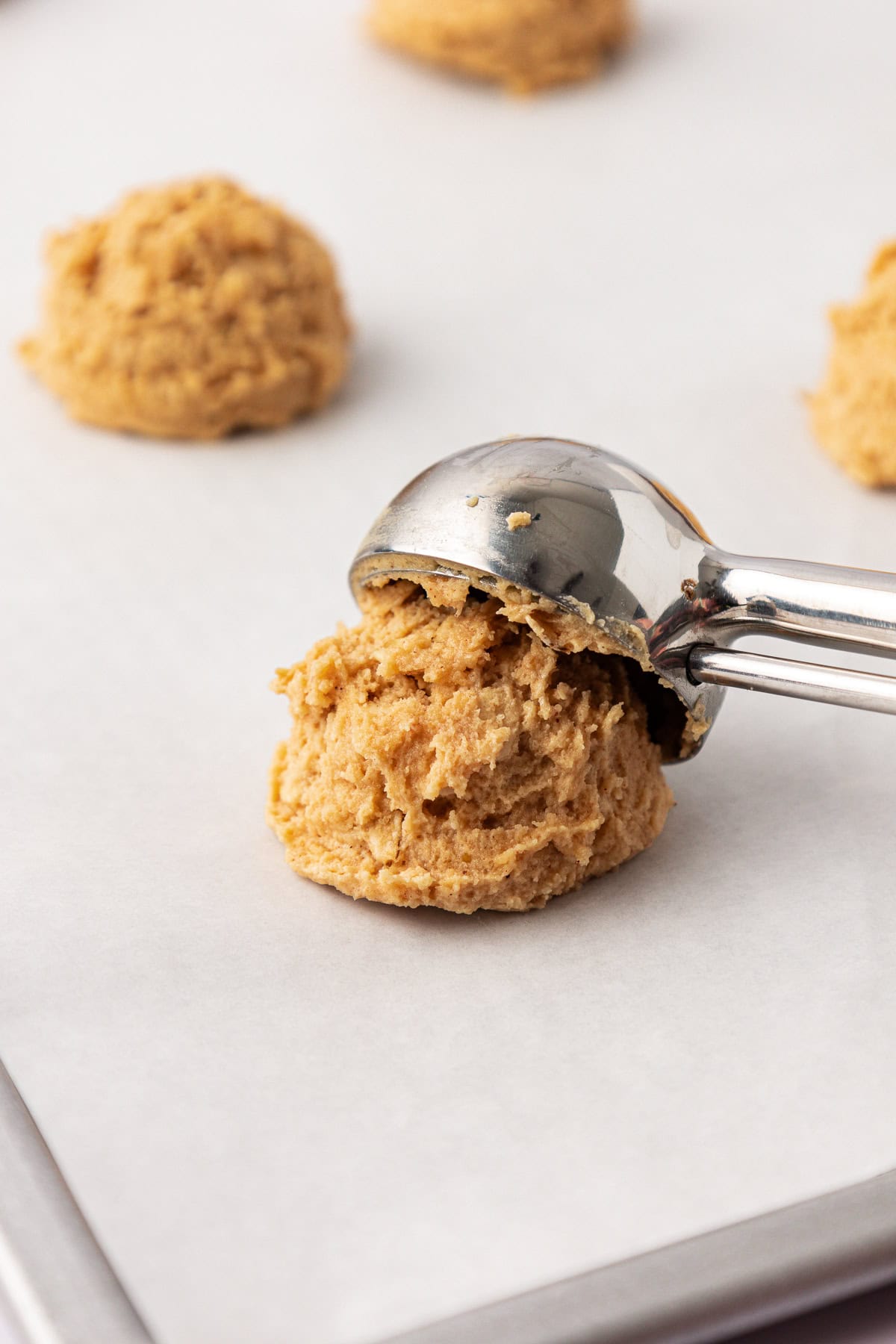 a cookie scoop placing a cookie dough ball on white parchment paper with more cooke dough balls in the background