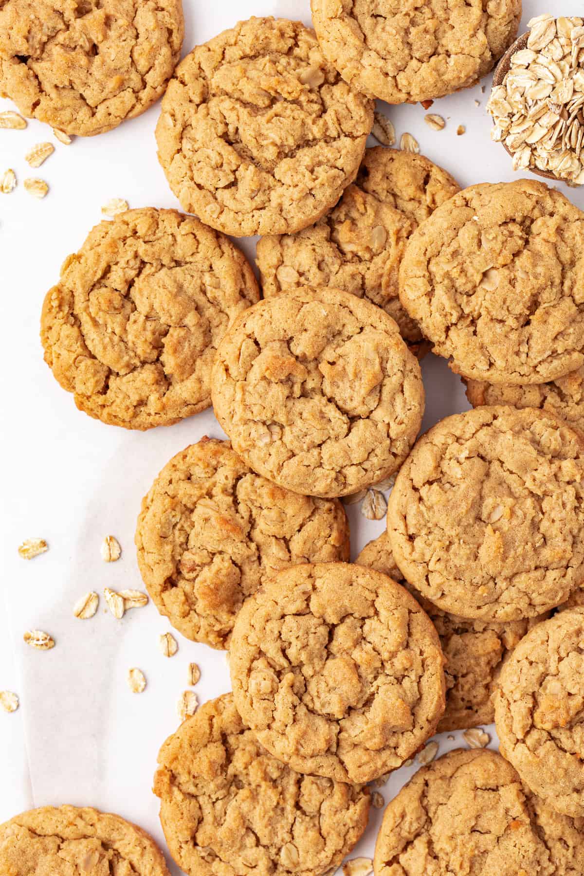 peanut butter oatmeal cookies scattered around on a white surface with oats scattered around