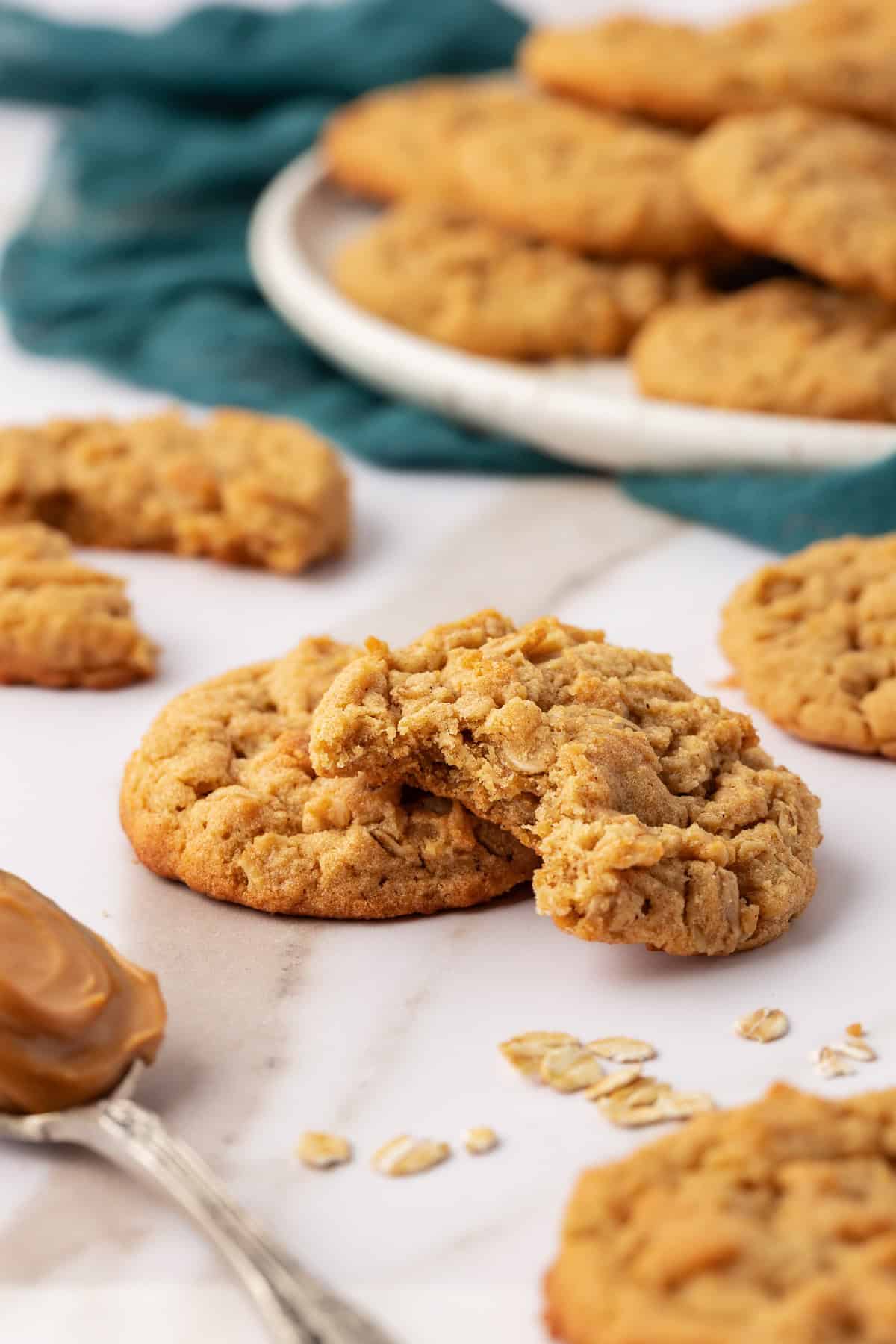 peanut butter oatmeal cookies scattered around, with one in the center missing a bite and leaning on top of another cookie, surrounded by oats and a spoonful of peanut butter