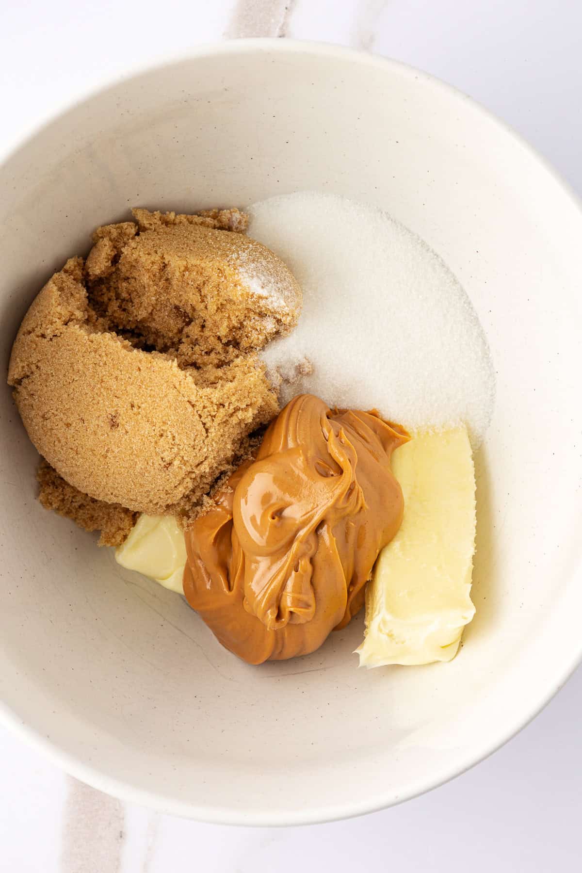 over head view of a white bowl with brown sugar, peanut butter, granulated sugar and butter in it