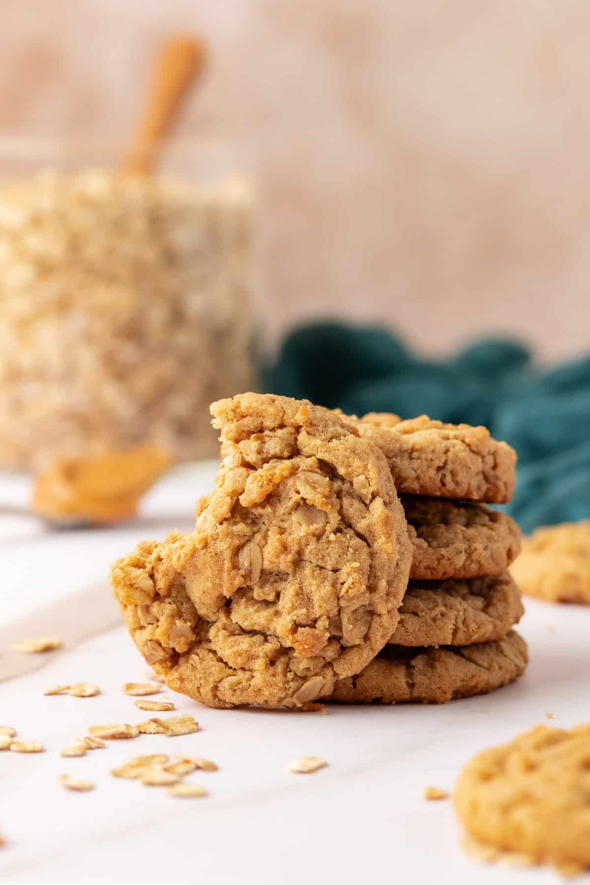 4 peanut butter oatmeal cookies stacked with one cookie leaning on it missing a bite, surrounded by scattered oats